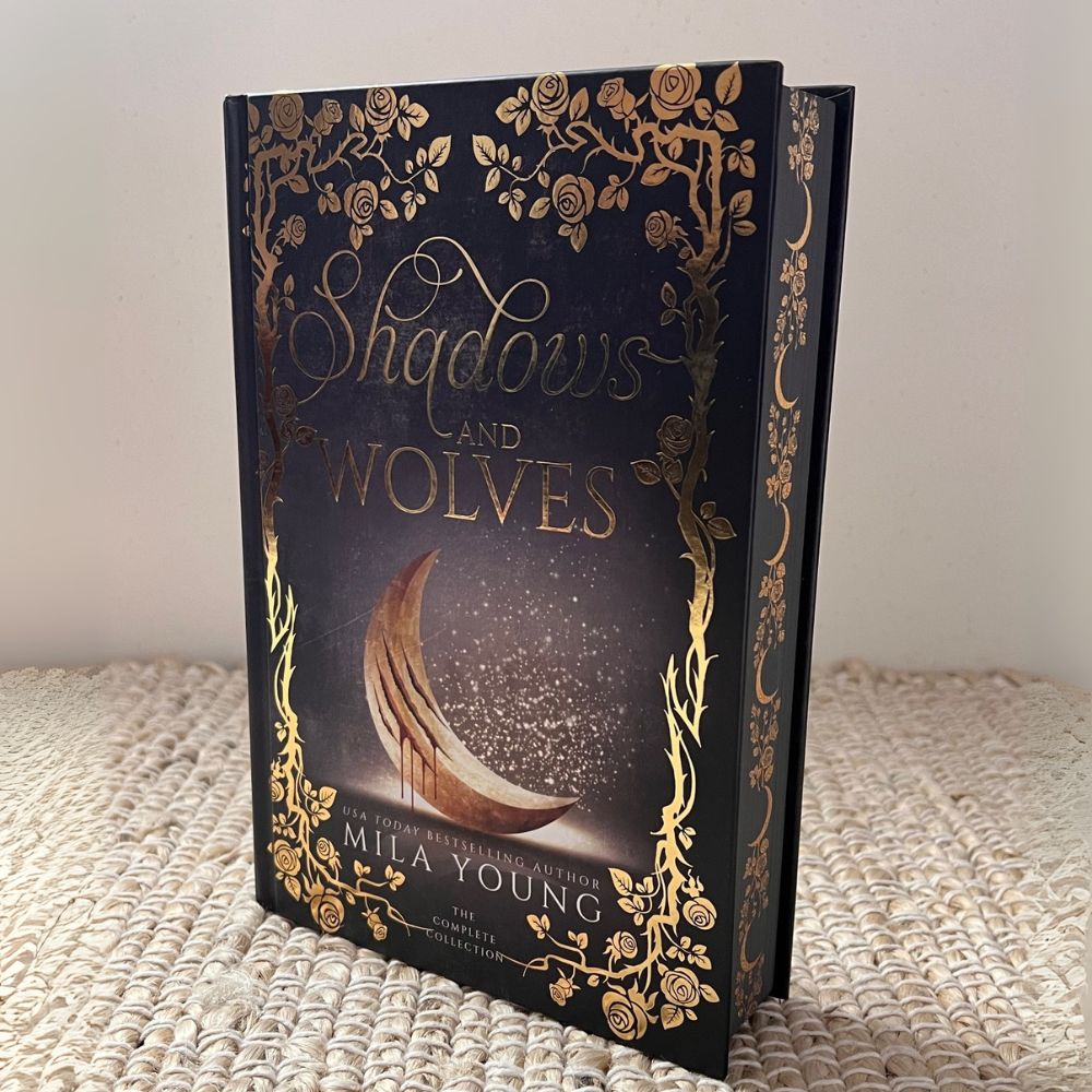 A damaged hardcover of Shadows & Wolves: Special Edition featuring gold foiled cover, metallic red page edges, illustrated interior artwork, and a vibrant full-colour bookmark, showcasing an enthralling paranormal romance with wolf shifters and a mysterious heroine